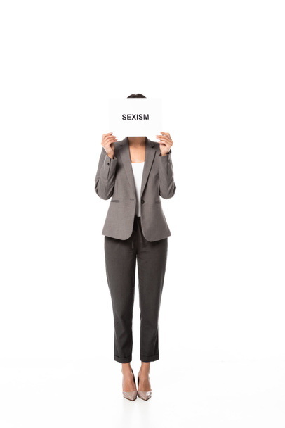 mujer de negocios en traje cubriendo la cara mientras sostiene la pancarta con letras de sexismo aisladas en blanco
 - Foto, Imagen
