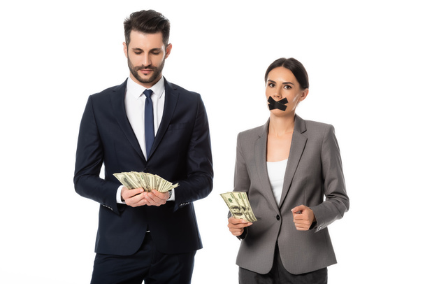 businessman holding dollars near businesswoman with duct tape on mouth standing  isolated on white - Photo, Image