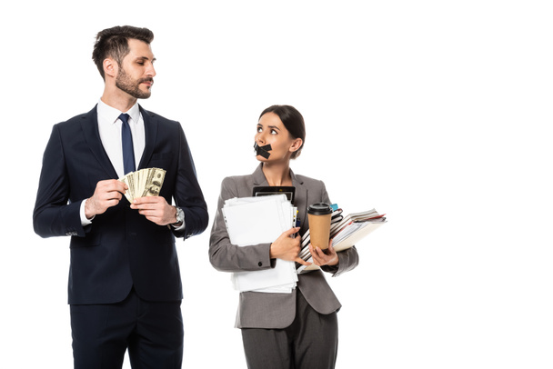 hombre de negocios guapo sosteniendo dólares y mirando a la mujer de negocios con cinta adhesiva en la boca aislado en blanco, concepto de sexismo
  - Foto, Imagen