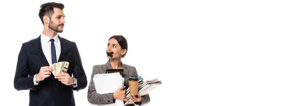 панорамний урожай гарного бізнесмена, що тримає долари біля бізнес-леді з стрічкою в роті ізольовано на білому, концепція сексизму
  - Фото, зображення