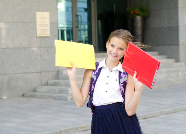 Back to school. Education concept. Cute smiling schoolgirl on the way to the school. Happy little girl child in uniform holding the books with backpack - 写真・画像