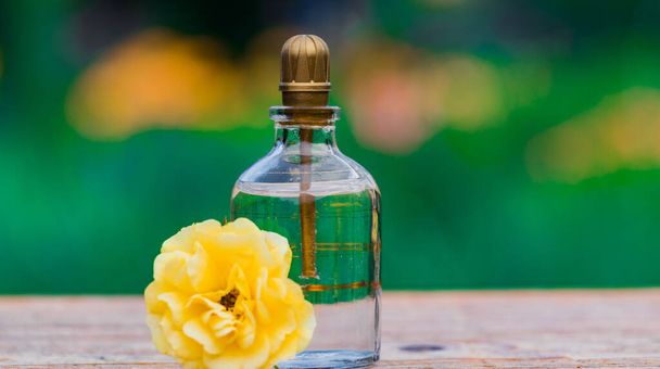 Frasco de perfume con flores sobre fondo claro. Botella de perfume con etiqueta y flores pequeñas sobre la mesa
. - Foto, Imagen