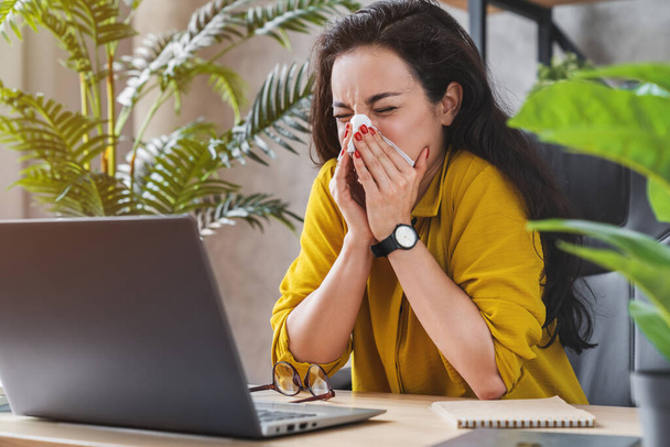 Young female worker blowing running nose got flu sneezing in tissue at workplace - Photo, image