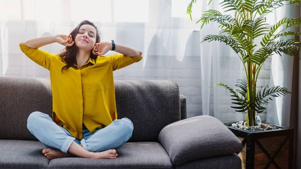 Joyful young woman stretching while sitting on sofa getting relaxed - Foto, immagini