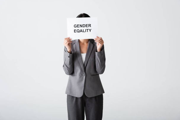 İş kadını yüzünü örterken elinde beyaz üzerine izole edilmiş cinsiyet eşitliği harfleri olan bir pankart tutuyor.  - Fotoğraf, Görsel