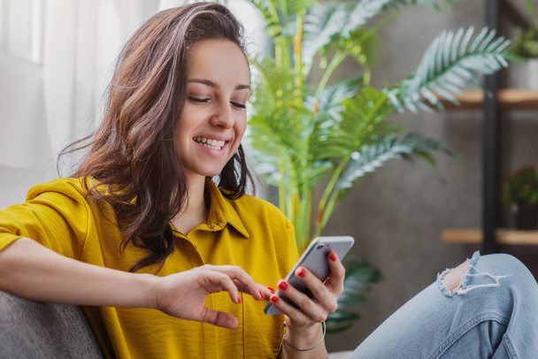 Young woman sitting relax on sofa in living room browsing internet on smartphone - Foto, immagini