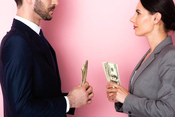 side view of businesswoman looking at businessman holding dollar banknotes on pink, gender equality concept  - Photo, Image
