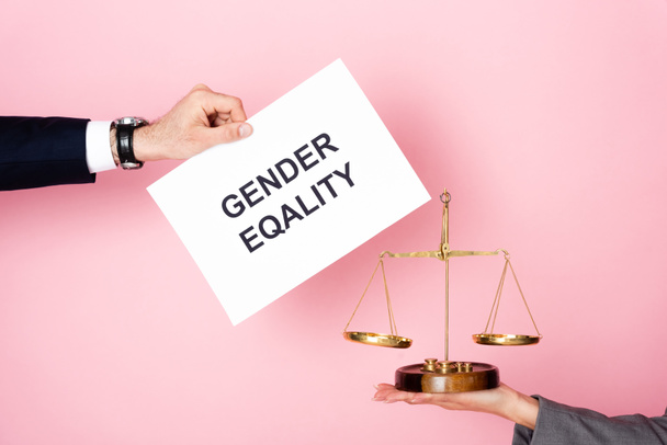 cropped view of businessman holding placard with gender equality lettering near businesswoman with golden scales on pink, gender equality concept  - Photo, Image