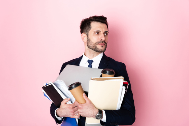 όμορφος επιχειρηματίας κρατώντας κύπελλα χαρτί, φορητό υπολογιστή, φακέλους και σημειωματάρια σε ροζ  - Φωτογραφία, εικόνα