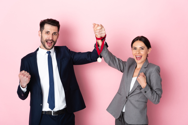 excited businessman and businesswoman holding golden medal and gesturing on pink, gender equality concept - Photo, Image