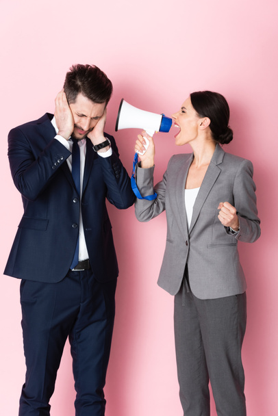 mujer emocional gritando en megáfono cerca de hombre de negocios cubriendo las orejas en rosa
  - Foto, Imagen