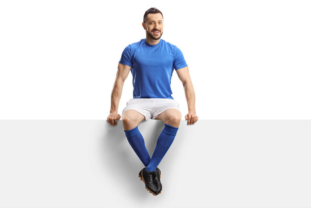 Soccer player sitting on a blank panel isolated on white background - Photo, Image