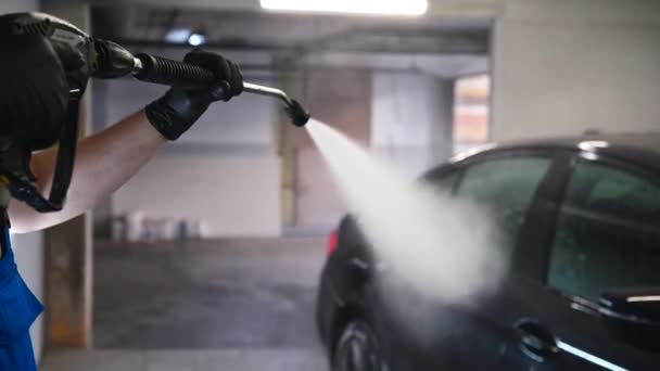 Lavagem de carro e detalhamento. Trabalhador profissional está lavando um carro preto por arruela de pressão em uma lavagem de carro. - Filmagem, Vídeo