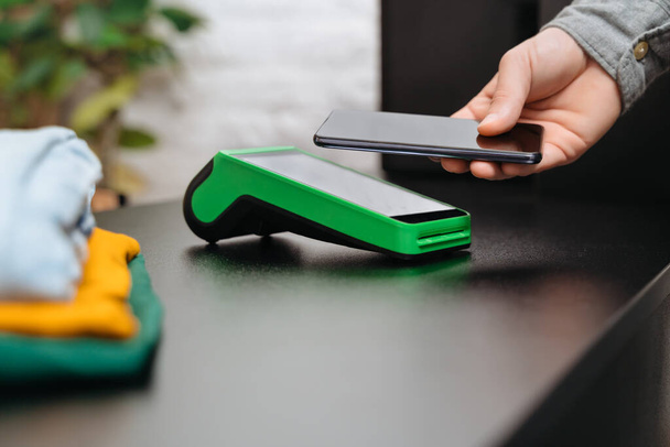 Клієнт платить за покупку в магазині одягу за допомогою смартфона, використовуючи сучасні технології НФК. NFC і концепція безконтактної оплати. Погляд зблизька - Фото, зображення