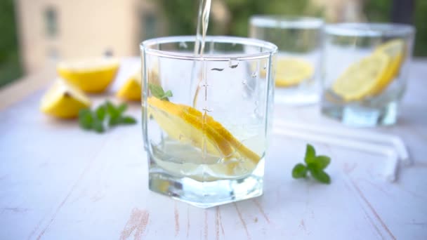Giet frisdrank water glas met ijs, munt en citroen. verfrissend zomercocktailconcept met tonic of transparante alcohol - Video
