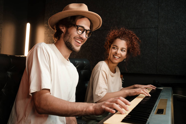 Giovani musicisti alla moda che suonano felicemente sulla tastiera del pianoforte registrando canzoni in un moderno studio di registrazione del suono - Foto, immagini