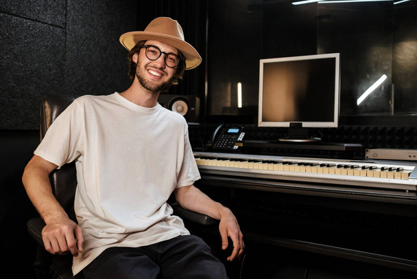 Handsome cheerful guy happily looking in camera in modern sound recording studio. Young stylish musician working in studio - Photo, Image