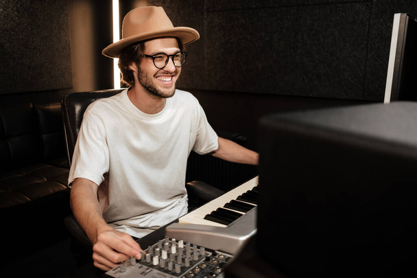 Mladý stylový veselý hudebník šťastně pracuje na novém albu v moderním nahrávacím studiu - Fotografie, Obrázek
