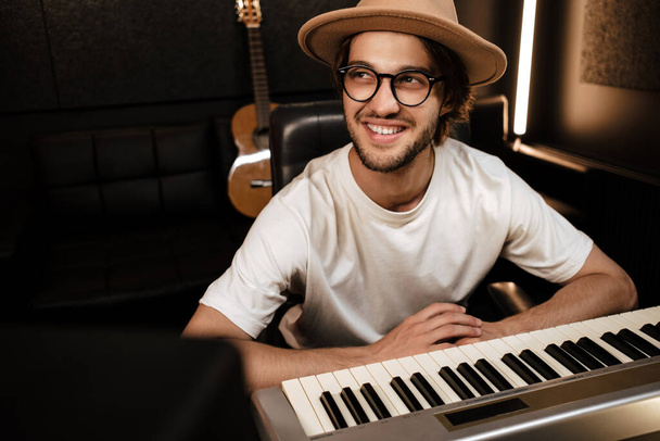 Young attractive stylish musician happily working in modern sound recording studio. Smiling man composing song in studio - Photo, Image