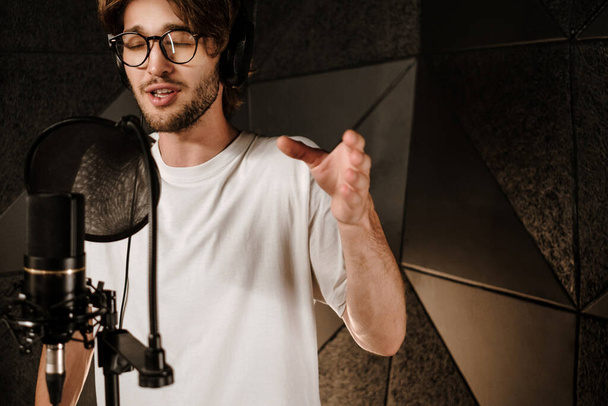 Portré fiatal férfi zenész fülhallgató érzékien énekel felvétel új dal a modern stúdióban  - Fotó, kép