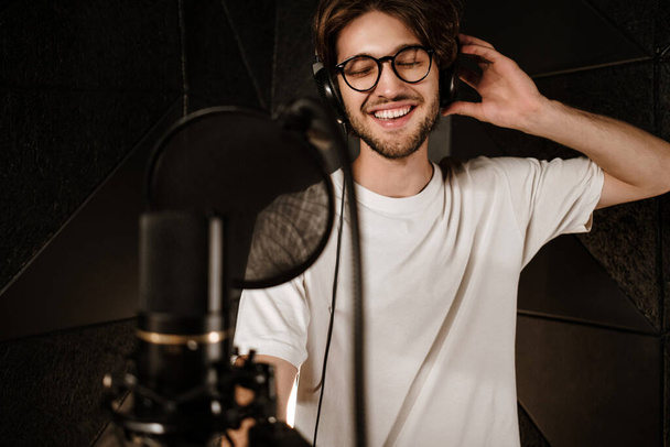 Joven cantante masculino atractivo en auriculares cantando alegremente en estudio de sonido moderno
  - Foto, imagen