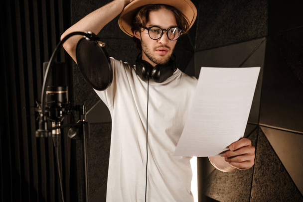 Jovem cantor masculino atencioso lendo atentamente o texto da nova música no estúdio de gravação de som moderno
  - Foto, Imagem