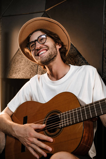 Przystojny uśmiechnięty muzyk z radością grający na gitarze nową piosenkę w studio nagraniowym - Zdjęcie, obraz