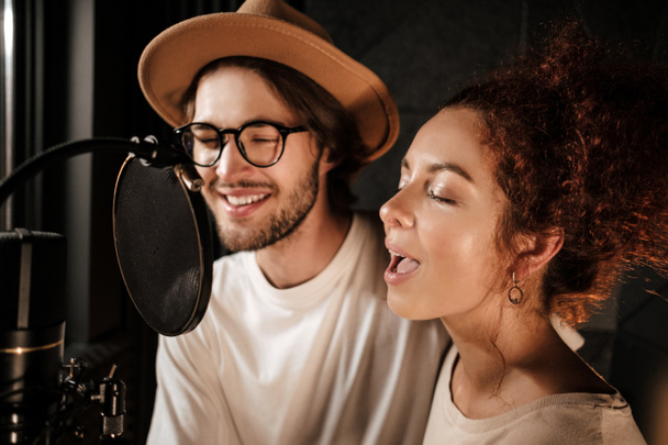 Jeunes musiciens attrayants chantant sensuellement ensemble sur un nouvel album de musique dans un studio d'enregistrement sonore moderne  - Photo, image