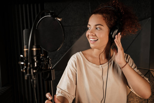 Kulaklıkla sesi dinleyen güzel bir bayan şarkıcı profesyonel stüdyoda yeni şarkılar kaydediyor.  - Fotoğraf, Görsel
