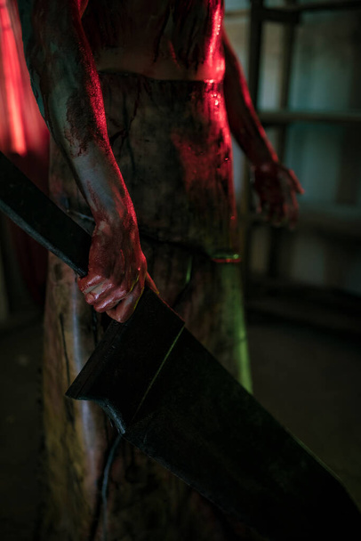 Dnipro, Oekraïne - 27 juni 2020: Cosplayer naar het beeld van beul Red Pyramid uit de horrorfilm "Silent Hill" staat in donkere kamer in schort met mes in zijn hand. Sluitingsdatum. - Foto, afbeelding