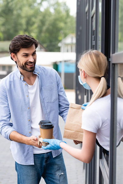 Selektiver Fokus des lächelnden und auf die Kellnerin blickenden Mannes, während er in der Nähe des Coffeeshops Bestellungen entgegennimmt  - Foto, Bild