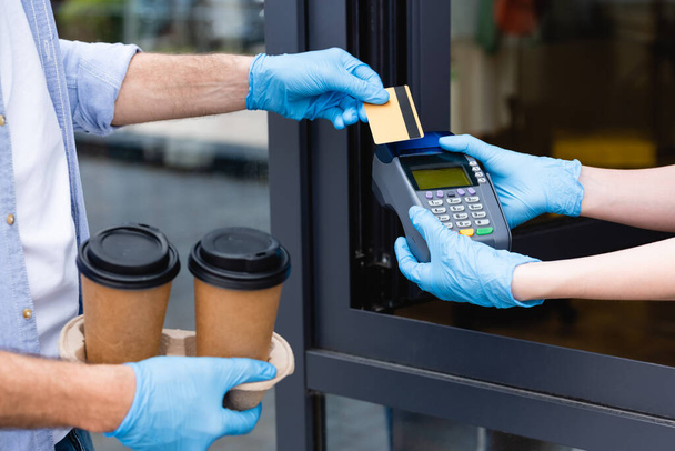 Vista cortada do homem que paga com cartão de crédito e garçonete segurando terminal de pagamento perto do café
  - Foto, Imagem