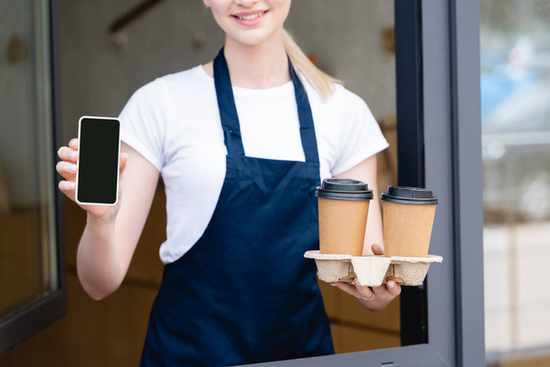 Vágott kilátás barista gazdaság papír poharak és okostelefon közelében kávézó - Fotó, kép