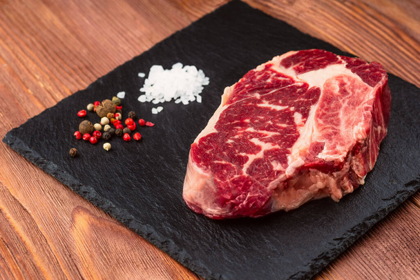 Fresh raw Prime Black Angus beef steaks on stone board: Striploin, Rib Eye. Top view. On a dark wood background - Photo, image