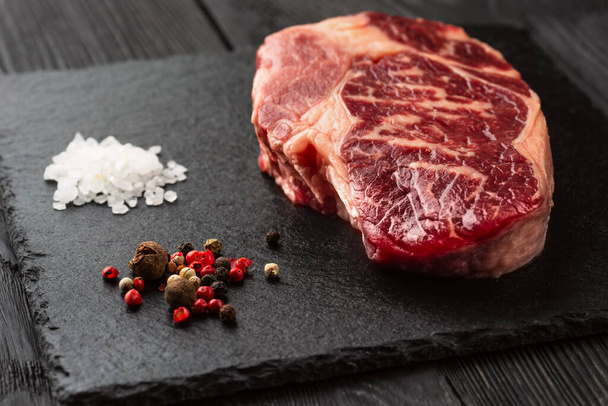 Fresh raw Prime Black Angus beef steaks on stone board: Striploin, Rib Eye. On a dark background - 写真・画像