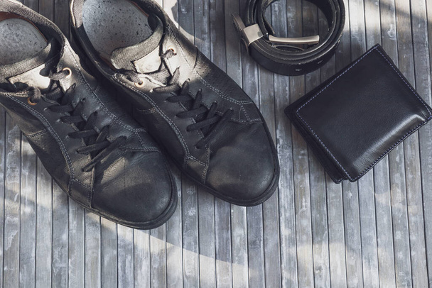 Black men's classic sneakers with belt and wallet on a gray wooden background, close-up top view. - Photo, Image