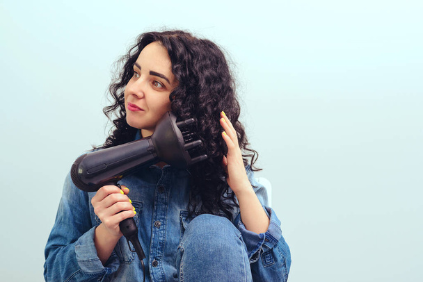 Woman using a modern hairdryer at home. Woman makes herself curly hairstyle. Beauty and haircare concept. Female drying hair. Girl styling her curly hair with hairdryer with special diffuser nozzle. - Photo, Image