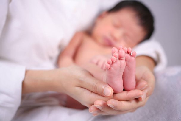 Η μητέρα κρατούσε το μωρό στο χέρι της. Η μαμά κρατάει μικρά ποδαράκια. Γυναίκα χέρια κρατώντας νεογέννητα πόδια του μωρού. - Φωτογραφία, εικόνα