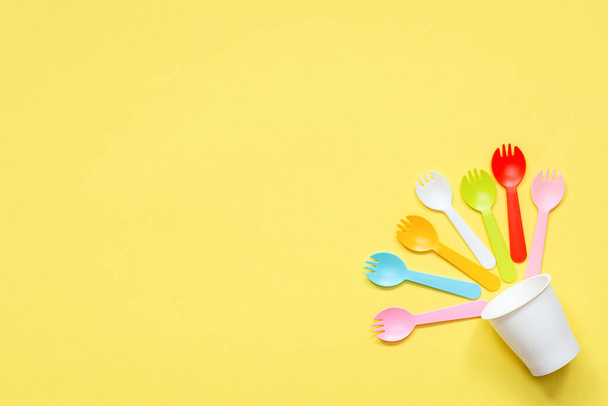 Flat lay of multi-colored plastic forks in white cup on bright yellow background with copy space. Minimal simple color style. Concept items for fast food. Copy space for your text.  - Photo, Image