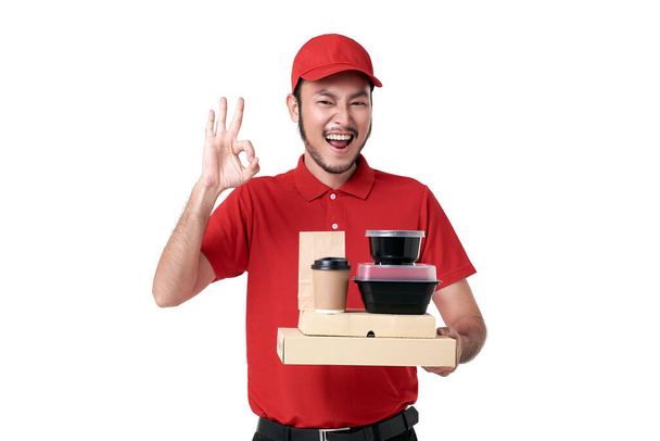Ασιάτης ντελιβεράς με κόκκινη στολή που κρατάει το κουτί του φαγητού και παίρνει τον καφέ απομονωμένο σε λευκό φόντο. υπηρεσία ταχείας παράδοσης κατά τη διάρκεια του covid19. - Φωτογραφία, εικόνα