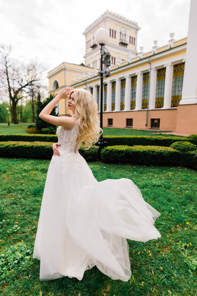 Young attractive blonde bride with curly hair walking in the park and smiling, concept wedding - Foto, Imagem