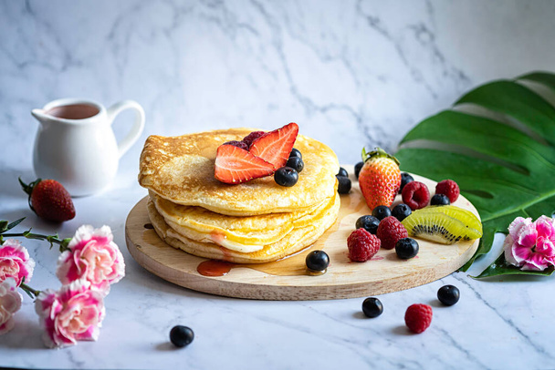 Delicious pancakes with fresh berries and honey on marble patterned floor with pink carnation and background. - Photo, Image