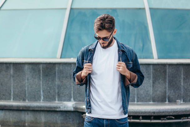 A young stylish man with a beard in a white T-shirt and glasses. Street photo - 写真・画像