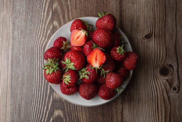 Fresh strawberries in a bowl on marble black table. Fresh nice strawberries. Juice strawberry. Strawberry field on fruit farm. Fresh ripe organic strawberry in white basket next to strawberries bed on pick your own berry plantation. - 写真・画像