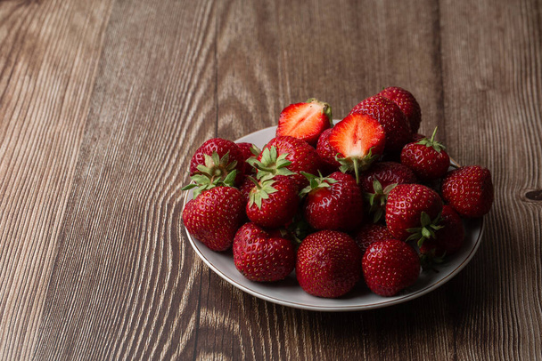 Frische Erdbeeren in einer Schüssel auf einem schwarzen Marmortisch. Frische schöne Erdbeeren. Erdbeersaft vorhanden. Erdbeerfeld auf Obstbauernhof. Frische reife Bio-Erdbeere im weißen Korb neben Erdbeerbeet auf der eigenen Beerenplantage pflücken. - Foto, Bild