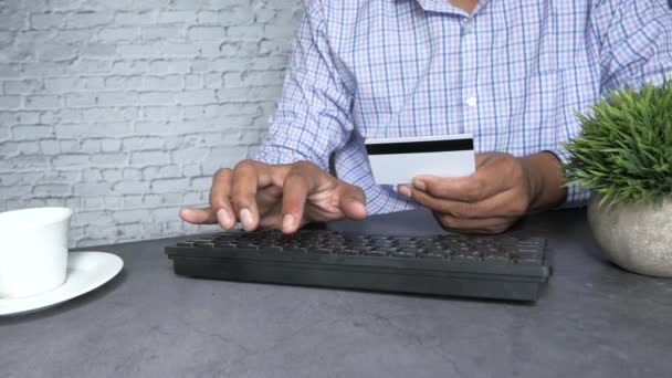 мужчина держит в руках кредитную карту и с помощью клавиатуры совершает покупки онлайн  - Кадры, видео