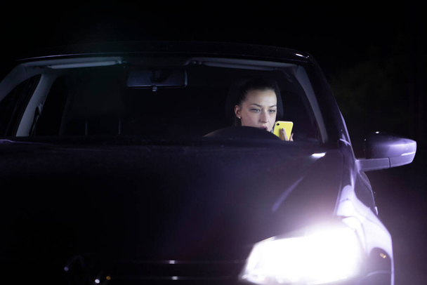 Σοκαρισμένη κοπέλα στο αυτοκίνητο χάνεται στο δρόμο τη νύχτα, φαίνεται στο κινητό τηλέφωνο πλοήγησης διαδρομή - Φωτογραφία, εικόνα