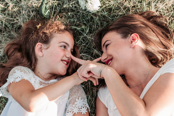 Mom and her daughter lying on the grass, touching noses and being playful with each other - Foto, afbeelding