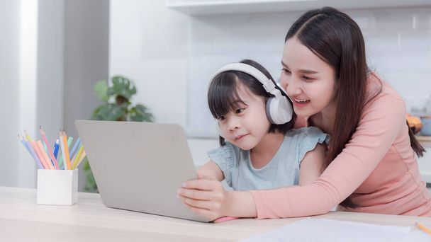 Ασιάτισσες μαμάδες και κορίτσια που σπουδάζουν online μέσω διαδικτύου χρησιμοποιώντας ένα φορητό υπολογιστή και ακούστε τον ήχο από τα ακουστικά - Φωτογραφία, εικόνα