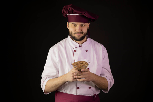młody uśmiechnięty Mistrz kuchni w mundurze trzyma miskę płatków zbożowych. naturalna koncepcja żywności - Zdjęcie, obraz